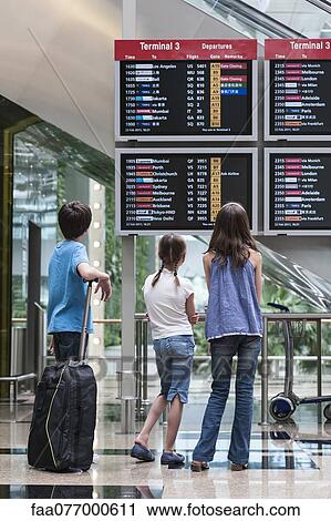 Stock Image - Children looking at arrival departure board, rear view. Fotosearch