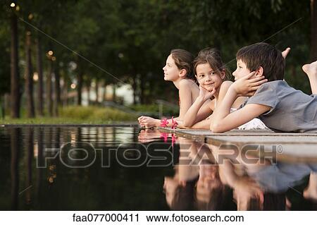 Stock Image - Children lying together at edge of pond. Fotosearch