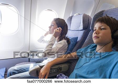 Stock Photograph - Children watching movie on airplane with headphones. Fotosearch