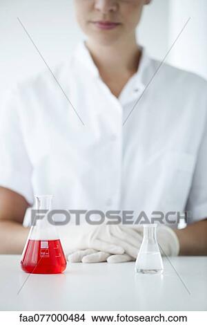 Picture - Conical flasks in laboratory, woman wearing latex gloves in background. Fotosearch