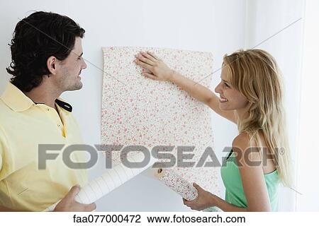 Stock Image - Couple decorating new house with wallpaper. Fotosearch