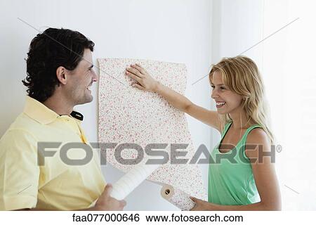 Stock Photograph - Couple decorating new house with wallpaper. Fotosearch