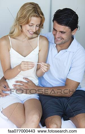 Stock Image - Couple looking at pregnancy test, man with hand on woman's abdomen. Fotosearch