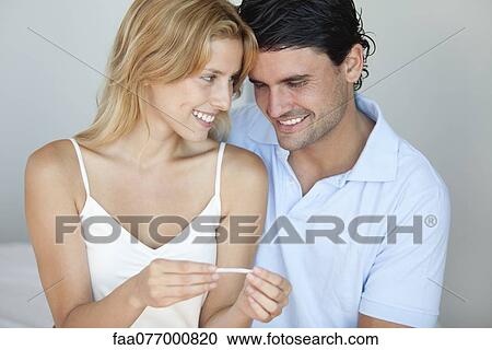 Stock Image - Couple looking at pregnancy test, smiling. Fotosearch