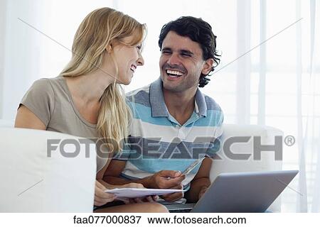 Couple shopping online with laptop, looking at each other laughing View Large Photo Image Stock Photo - Couple shopping online with laptop, looking at each other laughing. Fotosearch