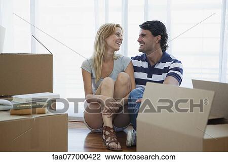 Stock Image - Couple sitting on floor in new house with cardboard boxes. Fotosearch