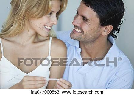 Couple smiling at each other, woman holding pregnancy test View Large Photo Image Stock Image - Couple smiling at each other, woman holding pregnancy test. Fotosearch