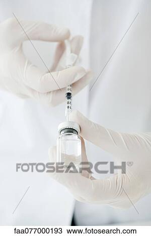 Stock Image - Extracting liquid from vial with syringe. Fotosearch