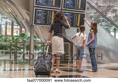 Stock Image - Family looking at arrival departure board in airport. Fotosearch