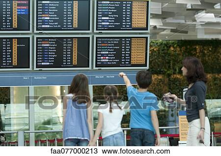 Stock Image - Family looking at arrival departure board, rear view. Fotosearch