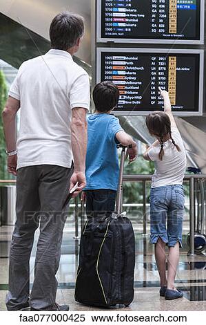 Stock Photography - Family looking at arrival departure board, rear view. Fotosearch