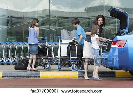 Stock Image - Family outside of airport unloading luggage from taxi trunk. Fotosearch