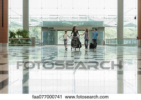Stock Image - Family pushing luggage cart in airport lobby. Fotosearch
