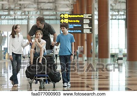 Stock Image - Family pushing luggage cart in airport. Fotosearch