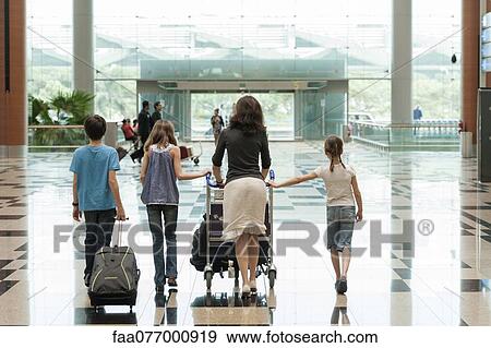 Stock Photo - Family pushing luggage cart in airport, rear view. Fotosearch