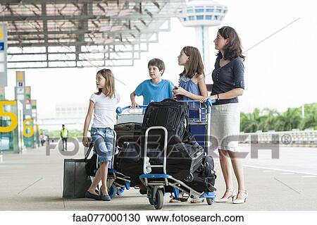 Stock Image - Family standing outside of airport with luggage. Fotosearch