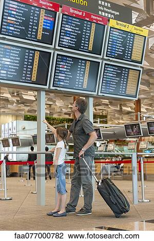 Stock Image - Father and daughter looking at arrival departure board in airport. Fotosearch