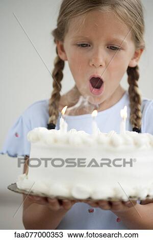 Stock Image - Girl blowing out candles on birthday cake. Fotosearch