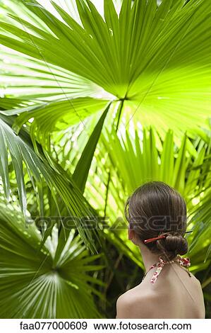Stock Photo - Girl contemplating palm leaves, rear view. Fotosearch