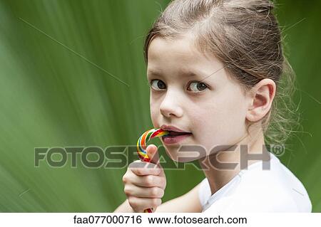Girl eating candy, looking over shoulder View Large Photo Image Stock Photograph - Girl eating candy, looking over shoulder. Fotosearch