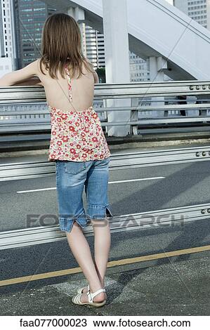 Stock Image - Girl leaning against railing on side of road. Fotosearch