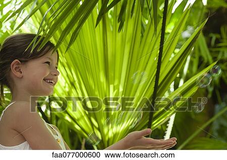 Stock Image - Girl playing with bubbles under palm leaves. Fotosearch