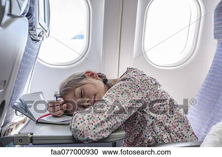 Stock Image - Girl resting head on tray table on airplane. Fotosearch