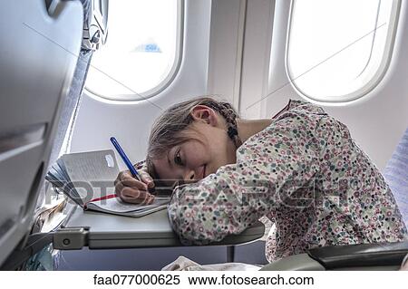 Stock Photography - Girl resting head on tray table on airplane, writing in diary. Fotosearch