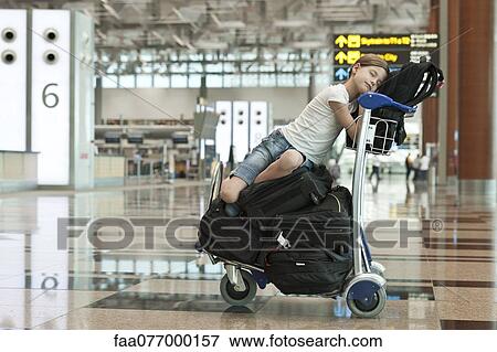 Stock Photo - Girl resting on top of luggage cart in airport. Fotosearch
