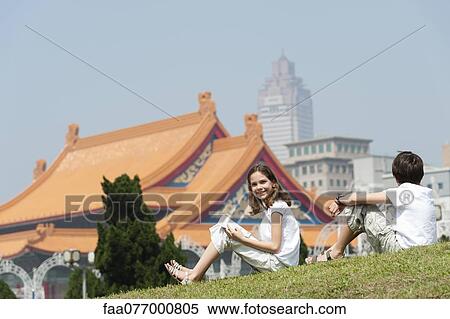 Stock Photography - Girl sitting on grass with brother near National Concert Hall, Chiang Kai-Shek Memorial Hall, Taipei, Taiwan. Fotosearch