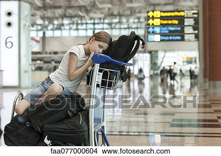 Picture - Girl sitting on top of luggage in airport. Fotosearch