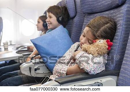 Stock Image - Girl sleeping on airplane holding stuffed animal. Fotosearch
