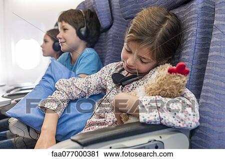 Stock Image - Girl sleeping on airplane holding stuffed toy. Fotosearch