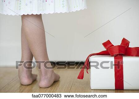 Stock Image - Girl standing beside wrapped gift, low section. Fotosearch