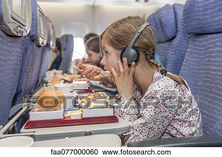 Girl watching movie on airplane while eating airline meal View Large Photo Image Stock Image - Girl watching movie on airplane while eating airline meal. Fotosearch