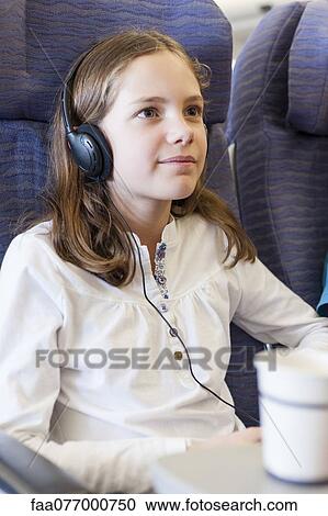Stock Image - Girl watching movie with headphones on airplane. Fotosearch