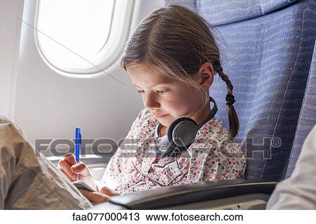 Stock Image - Girl writing in notebook on airplane. Fotosearch