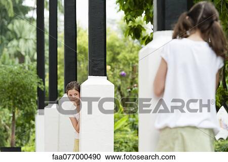 Stock Image - Girls playing hide-and-seek outdoors. Fotosearch