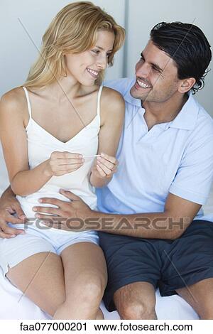 Stock Image - Husband putting hand on wife's abdomen after reading result of pregnancy test. Fotosearch