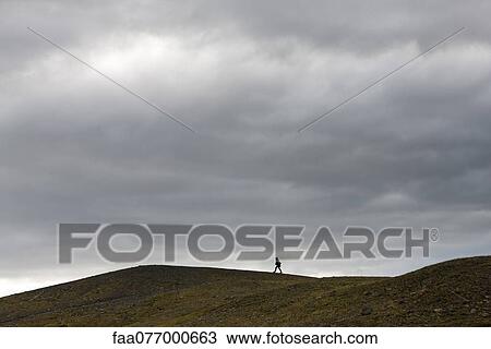 Stock Image - Iceland, person walking along barren hilltop. Fotosearch