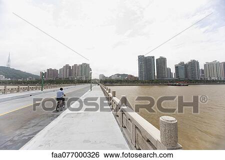 Stock Photograph - Man riding bicycle on bridge, Shandong province, China. Fotosearch