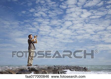 Stock Photograph - Man standing alone on breakwater, shouting into megaphone. Fotosearch