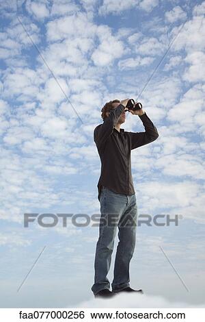 Stock Photograph - Man standing on cloud, looking through binoculars. Fotosearch