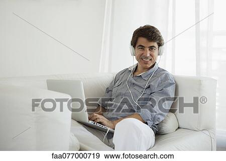 Mature man using laptop computer on sofa wearing headphones View Large Photo Image Stock Photo - Mature man using laptop computer on sofa wearing headphones. Fotosearch