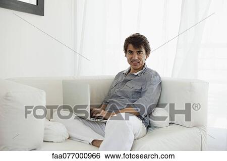 Stock Photograph - Mature man using laptop computer on sofa, portrait. Fotosearch