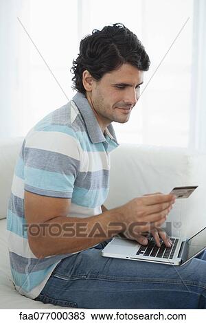Mid-adult man holding credit card while using laptop computer View Large Photo Image Stock Image - Mid-adult man holding credit card while using laptop computer. Fotosearch