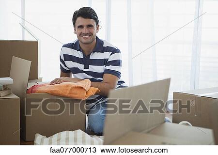 Stock Image - Mid-adult man unpacking in new house. Fotosearch
