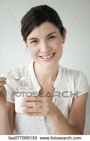 Stock Photography - Mid-adult woman eating yogurt, portrait. Fotosearch