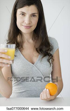 Picture - Mid-adult woman holding glass of orange juice and fresh orange. Fotosearch