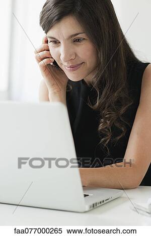 Stock Photography - Mid-adult woman using cell phone and laptop. Fotosearch